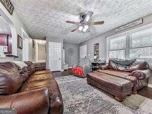 living room featuring ceiling fan, dark wood-type flooring, and a textured ceiling