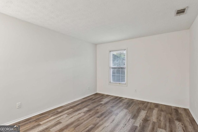 spare room featuring visible vents, a textured ceiling, baseboards, and wood finished floors