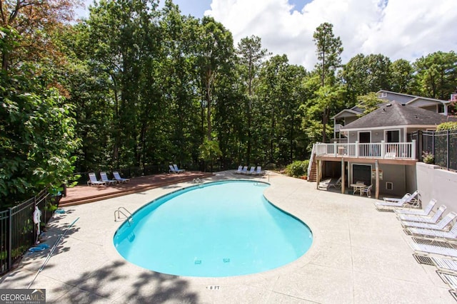 community pool with a wooden deck, fence, stairs, and a patio area
