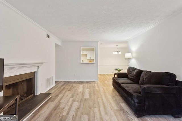 living room with crown molding, light wood-type flooring, a textured ceiling, and a notable chandelier