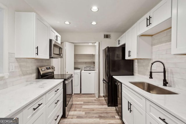 kitchen with a sink, appliances with stainless steel finishes, white cabinets, and independent washer and dryer