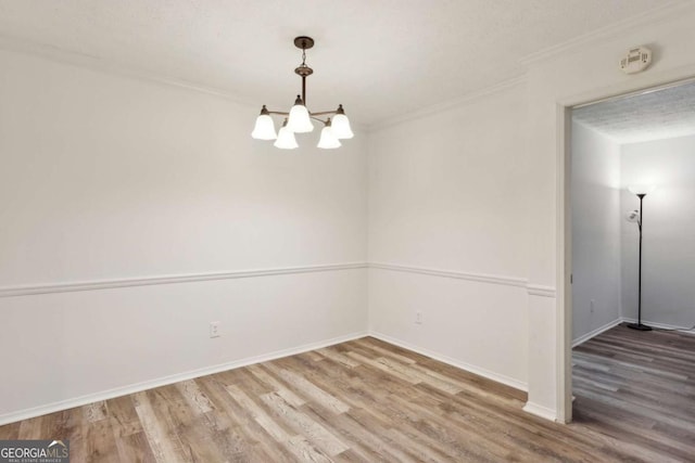 unfurnished room with crown molding, baseboards, wood finished floors, and a chandelier