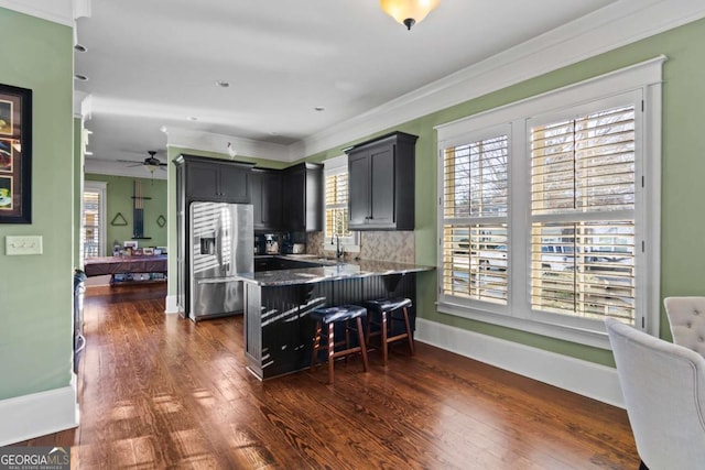 kitchen featuring crown molding, decorative backsplash, stainless steel refrigerator with ice dispenser, kitchen peninsula, and a breakfast bar