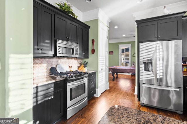 kitchen with crown molding, dark hardwood / wood-style flooring, tasteful backsplash, light stone countertops, and stainless steel appliances