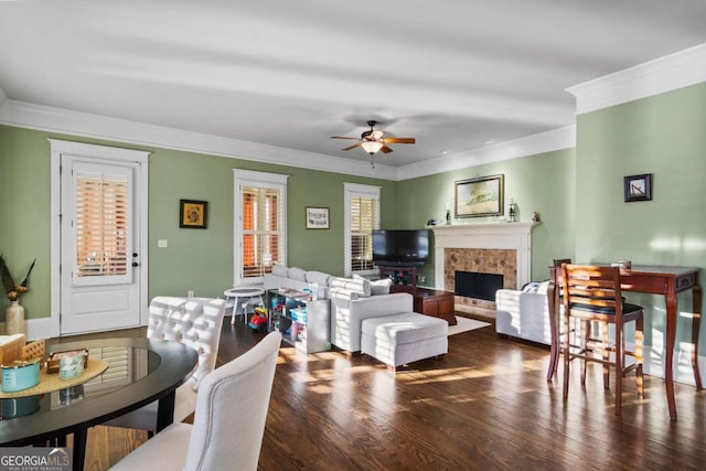 living room with ceiling fan, dark wood-type flooring, a tile fireplace, and crown molding