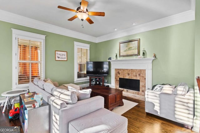 living room with ceiling fan, crown molding, dark hardwood / wood-style flooring, and a tiled fireplace