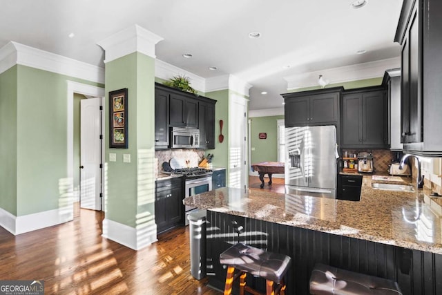 kitchen with appliances with stainless steel finishes, sink, light stone counters, a kitchen bar, and decorative backsplash