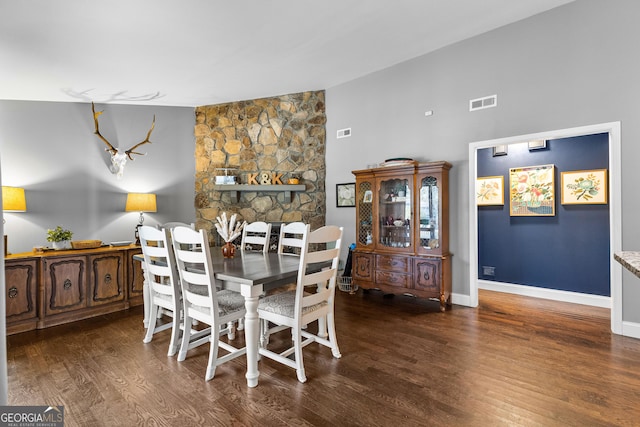 dining room with a stone fireplace and dark wood-type flooring