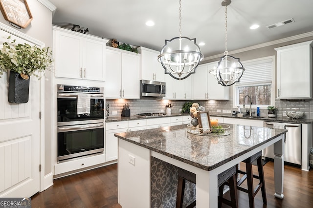 kitchen with a kitchen island, appliances with stainless steel finishes, hanging light fixtures, and white cabinets