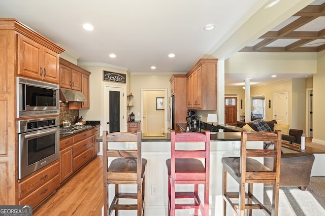 kitchen featuring a kitchen bar, stainless steel appliances, ornate columns, ornamental molding, and beam ceiling