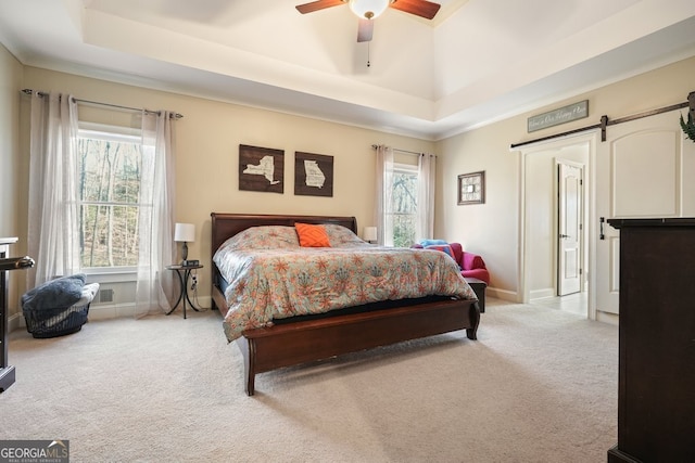 carpeted bedroom featuring ceiling fan, a barn door, and a tray ceiling