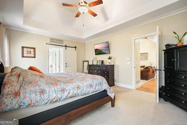 carpeted bedroom with ceiling fan, a barn door, ornamental molding, and a tray ceiling