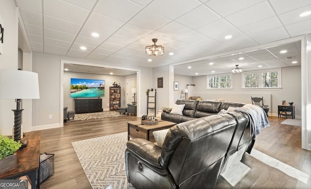 living room featuring a paneled ceiling, a notable chandelier, and light wood-type flooring