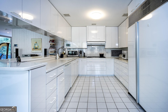 kitchen featuring sink, light tile patterned floors, paneled built in fridge, white cabinets, and kitchen peninsula