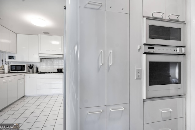 kitchen featuring tasteful backsplash, white appliances, light tile patterned flooring, and white cabinets