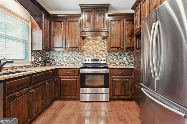 kitchen featuring stainless steel appliances, light stone countertops, sink, and backsplash