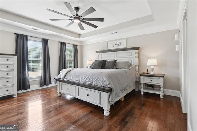 bedroom with a raised ceiling, dark wood-type flooring, and ceiling fan