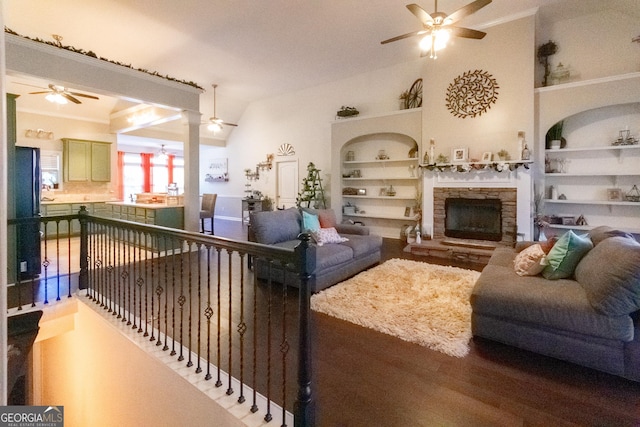 living room featuring vaulted ceiling, ceiling fan, built in features, hardwood / wood-style flooring, and a stone fireplace