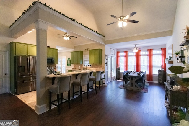 kitchen with kitchen peninsula, stainless steel fridge, a kitchen bar, high vaulted ceiling, and green cabinetry