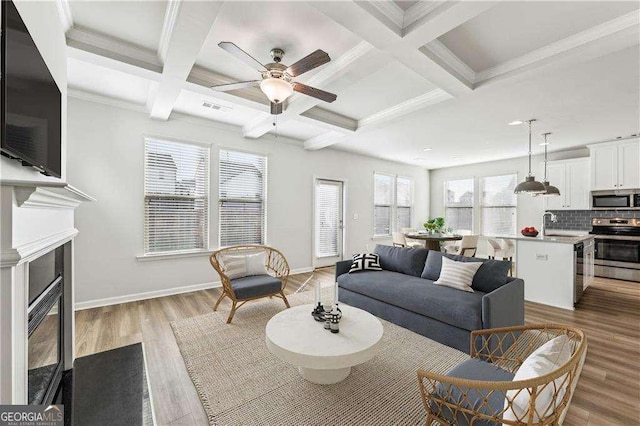 living room with beamed ceiling, crown molding, coffered ceiling, sink, and light hardwood / wood-style flooring