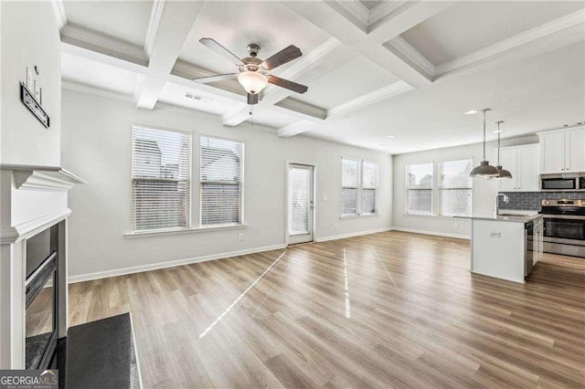 unfurnished living room with light wood-type flooring, coffered ceiling, beamed ceiling, and a healthy amount of sunlight