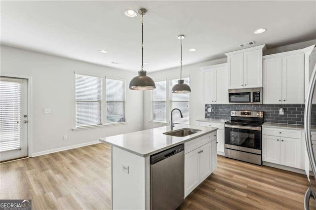 kitchen featuring appliances with stainless steel finishes, sink, decorative light fixtures, white cabinetry, and a center island with sink