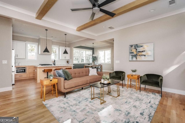 living room featuring plenty of natural light, light hardwood / wood-style flooring, beamed ceiling, and ceiling fan