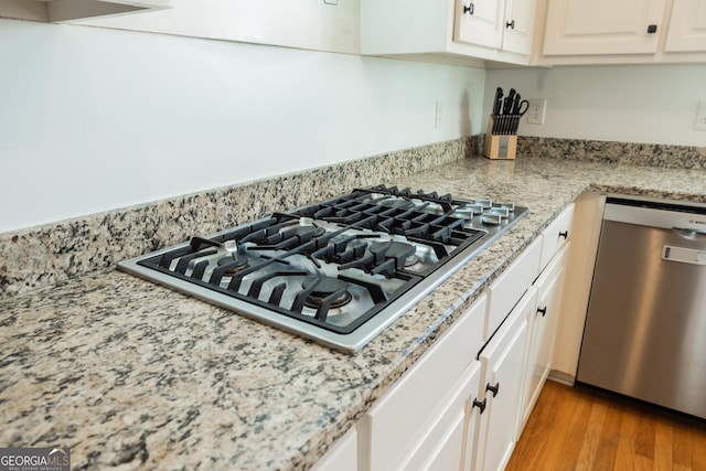 kitchen with white cabinets, light hardwood / wood-style floors, light stone countertops, and appliances with stainless steel finishes