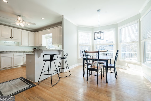 kitchen featuring crown molding, white cabinetry, hanging light fixtures, a breakfast bar, and light stone counters