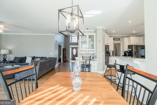 dining space with light hardwood / wood-style floors, crown molding, and ceiling fan with notable chandelier