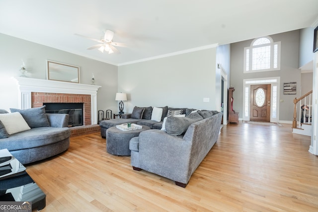 living room with ceiling fan, a brick fireplace, ornamental molding, and light hardwood / wood-style floors