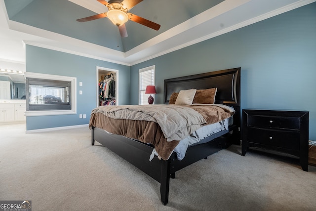 carpeted bedroom with ceiling fan, ensuite bathroom, a raised ceiling, and a spacious closet