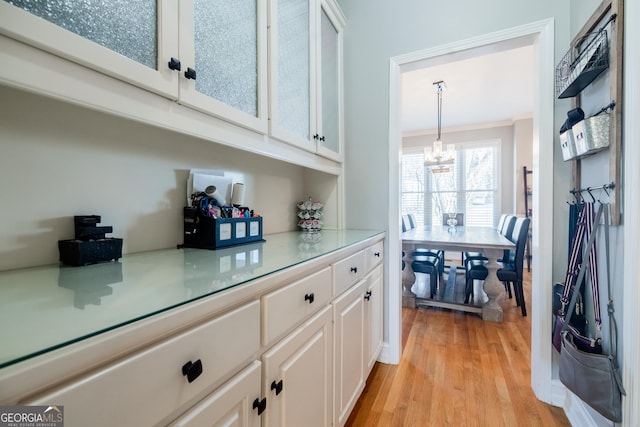 bar with decorative light fixtures, white cabinets, light hardwood / wood-style flooring, and crown molding