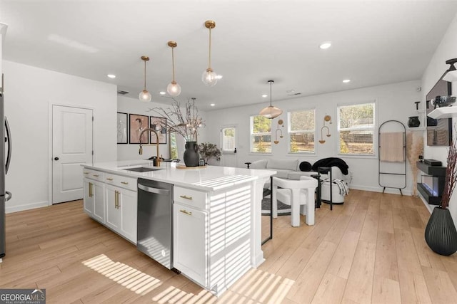 kitchen with white cabinetry, sink, hanging light fixtures, stainless steel dishwasher, and a center island with sink