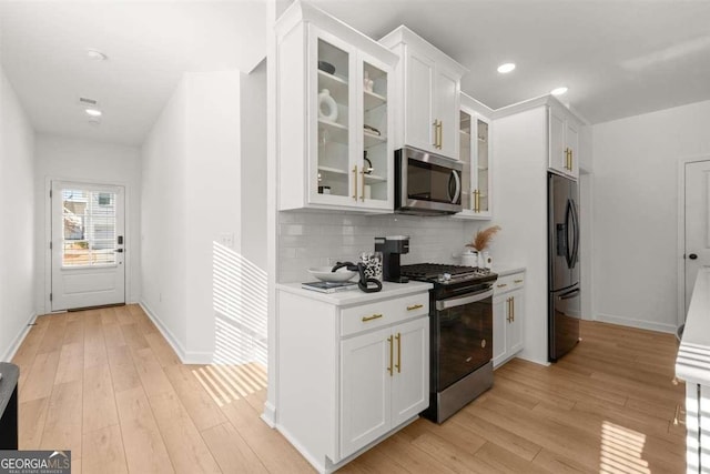 kitchen featuring white cabinets, stainless steel appliances, light wood-type flooring, and tasteful backsplash