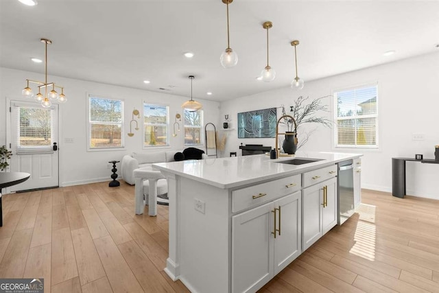 kitchen featuring a kitchen island with sink, sink, decorative light fixtures, white cabinets, and a healthy amount of sunlight