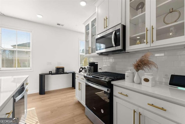 kitchen featuring light stone countertops, appliances with stainless steel finishes, white cabinetry, tasteful backsplash, and light wood-type flooring