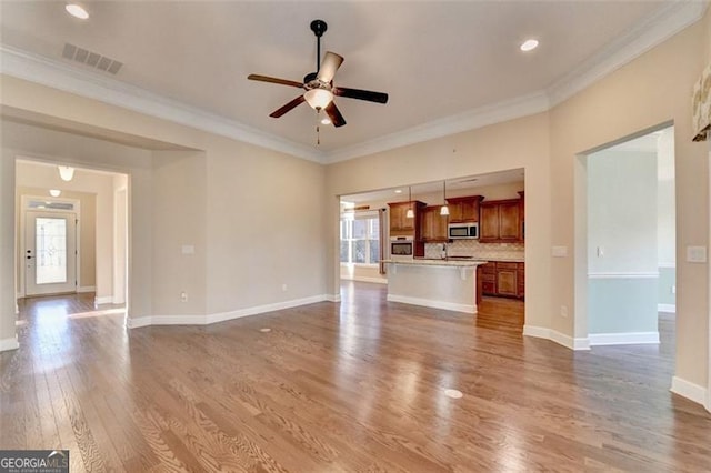 unfurnished living room featuring plenty of natural light, wood finished floors, visible vents, and crown molding