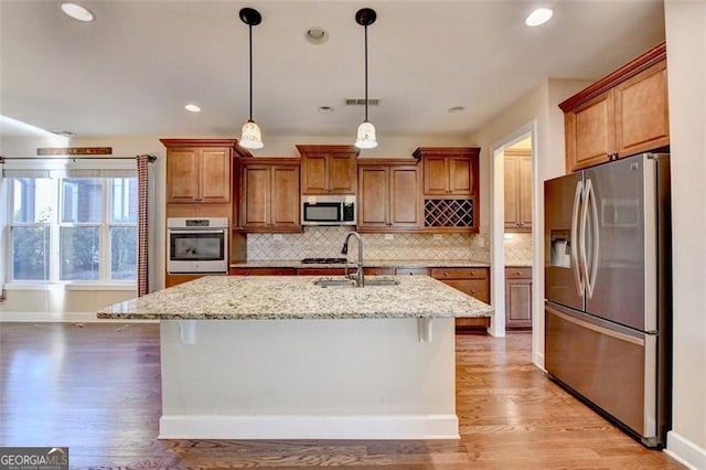 kitchen featuring appliances with stainless steel finishes, a sink, light wood-style flooring, and decorative backsplash