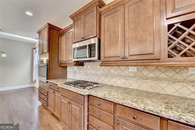 kitchen with light stone counters, stainless steel appliances, baseboards, decorative backsplash, and light wood finished floors