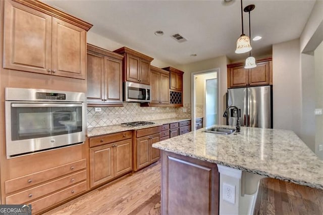 kitchen featuring visible vents, light stone counters, appliances with stainless steel finishes, a sink, and backsplash