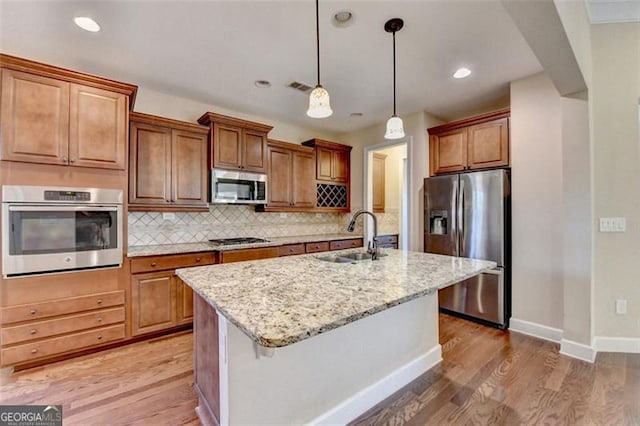 kitchen with light wood-type flooring, appliances with stainless steel finishes, decorative backsplash, and a sink