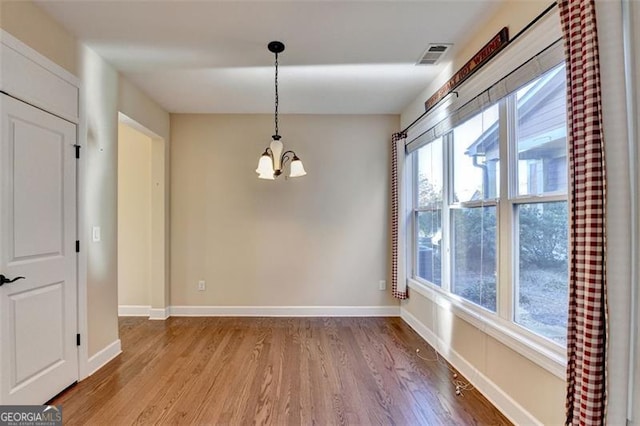 unfurnished dining area with a chandelier, wood finished floors, visible vents, and a healthy amount of sunlight