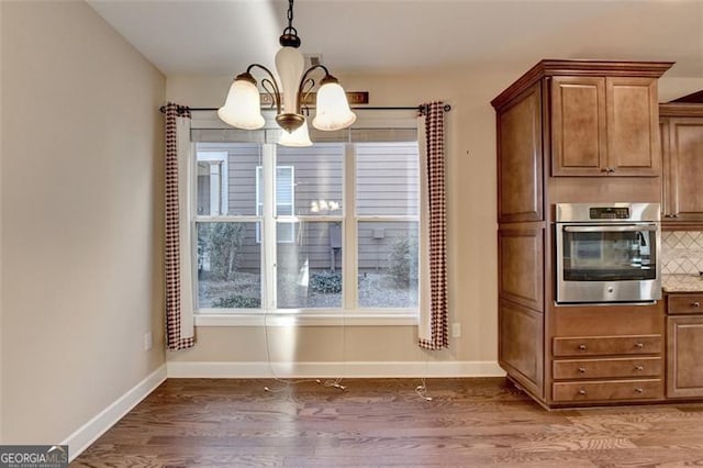 kitchen with light wood finished floors, tasteful backsplash, baseboards, oven, and a notable chandelier