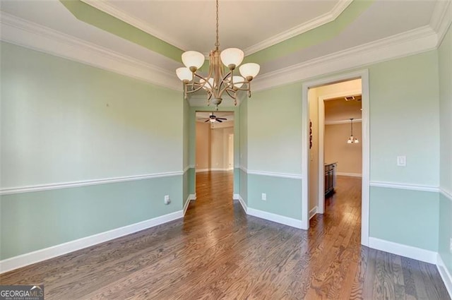 unfurnished dining area featuring a tray ceiling, crown molding, wood finished floors, baseboards, and ceiling fan with notable chandelier