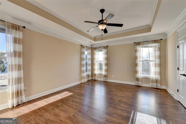 empty room with a raised ceiling, ornamental molding, a ceiling fan, wood finished floors, and baseboards