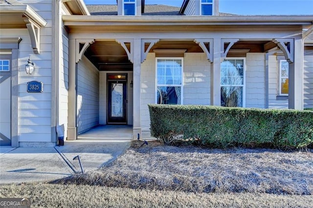 view of exterior entry with covered porch and roof with shingles