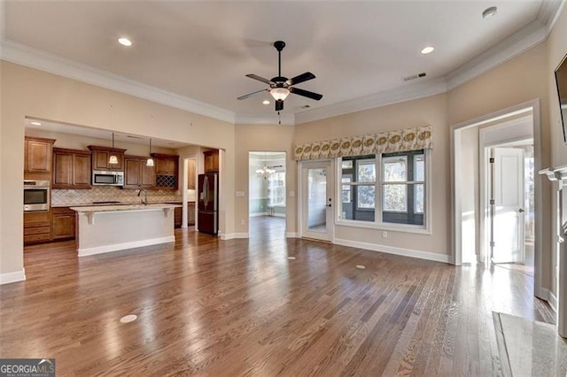 unfurnished living room with dark wood-style flooring, a ceiling fan, baseboards, visible vents, and crown molding