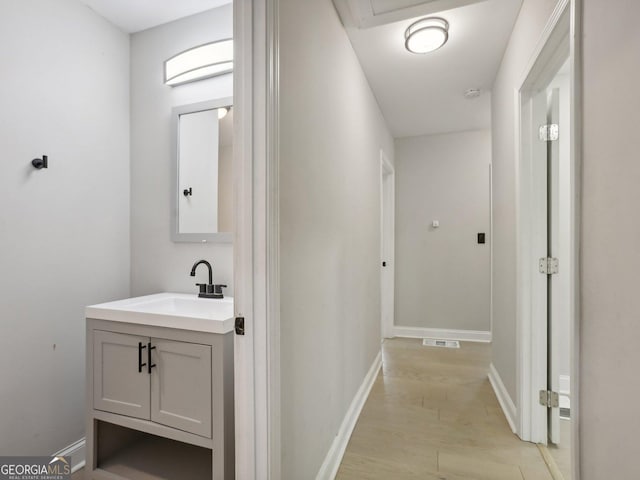 hall with visible vents, light wood-type flooring, baseboards, and a sink