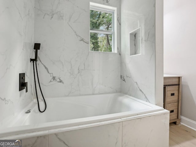 bathroom featuring baseboards, a tub with marble appearance, and vanity